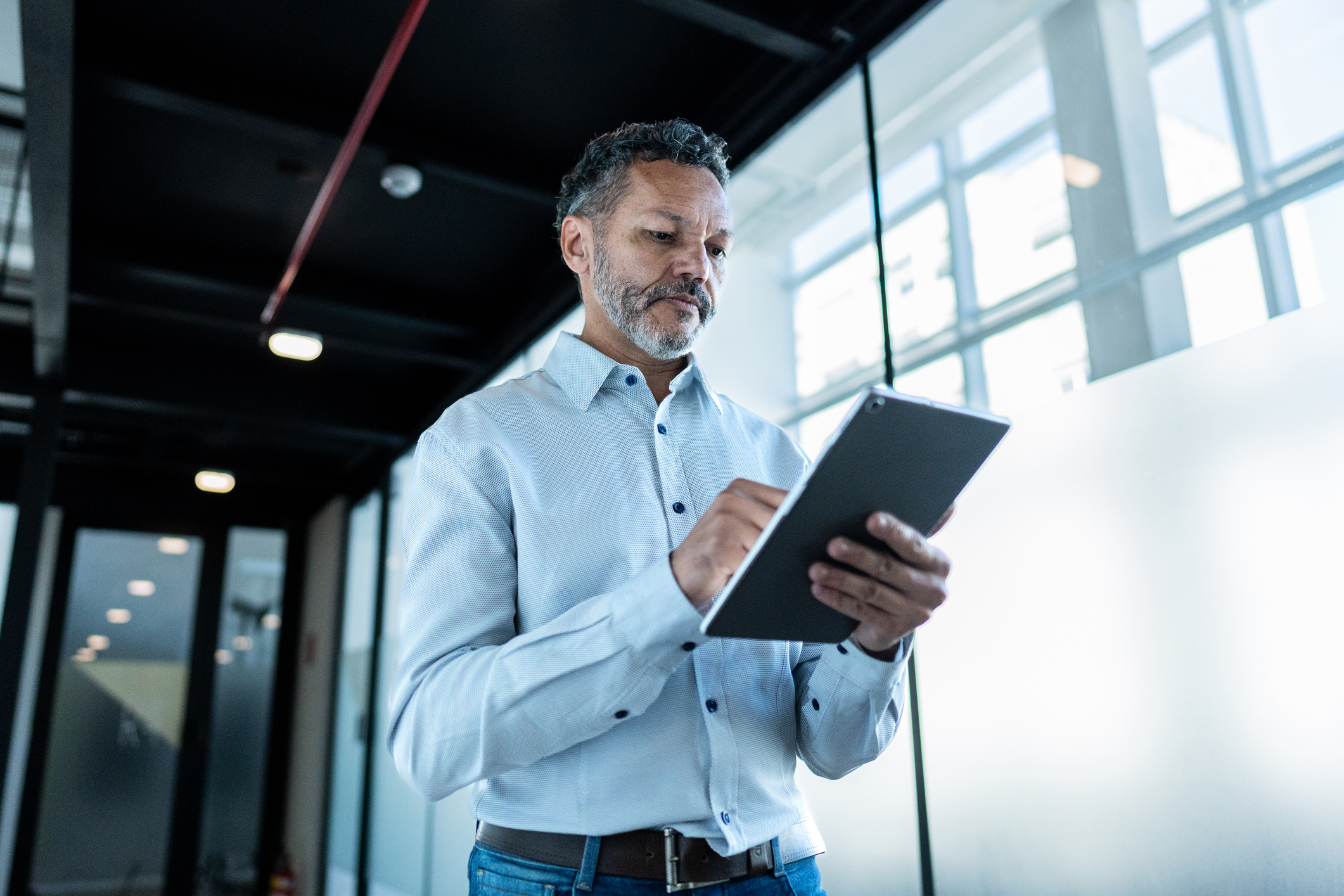 Mature businessman using digital tablet and walking at office