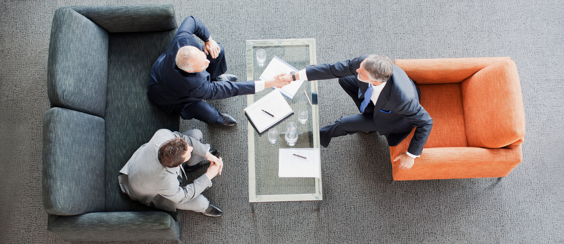 Businessmen shaking hands across coffee table in office lobby