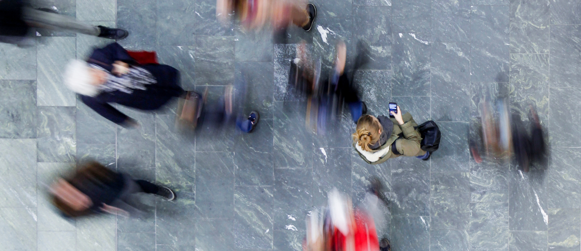Aerial view of woman standing and looking on her smartphone, surrounded by walking people.