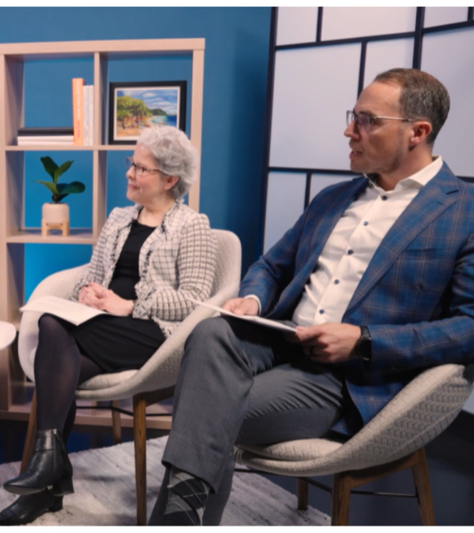 Two people sit in an interview talking to a panel moderator.