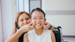 Portrait of Asian little illness girl sitting on wheelchair with smiling in hospital while waiting for medical service. The young kid feeling good, hopeful and cheerful making with happy face.