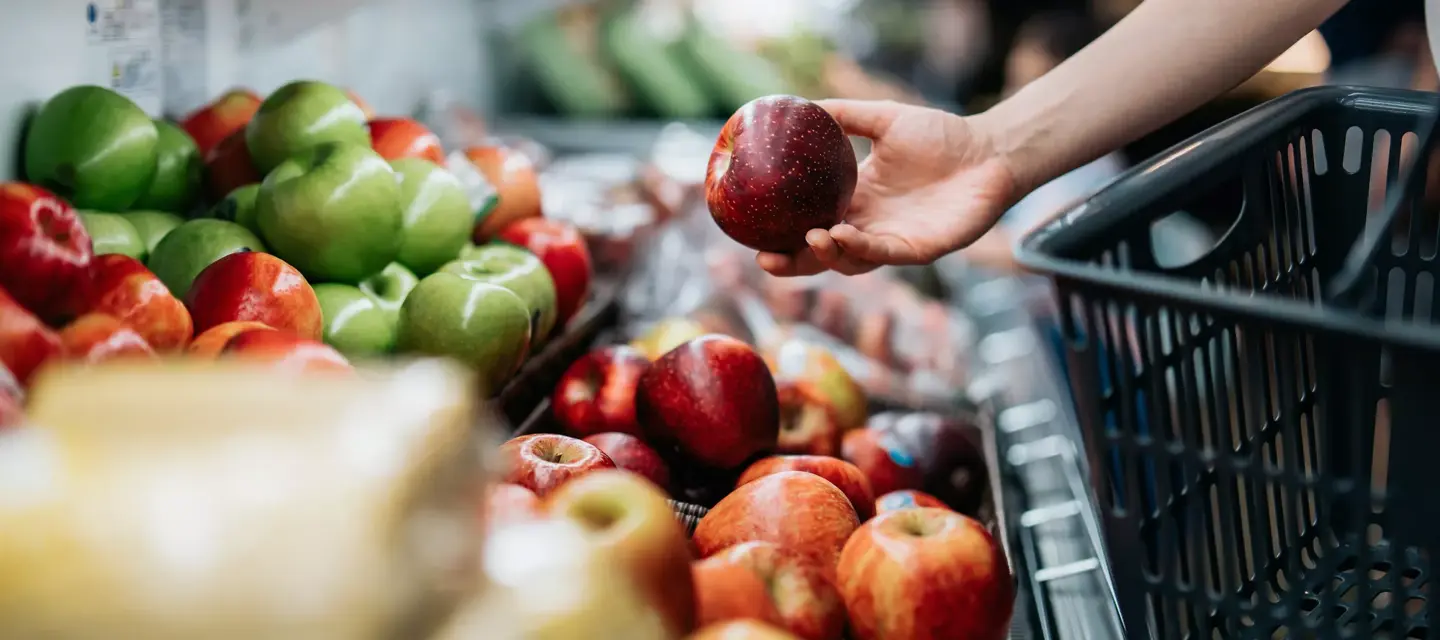 Cropped shot of young Asian woman choosing fresh organic fruits in supermarket. She is picking a red apple along the produce aisle. Routine grocery shopping. Healthy living and eating lifestyle