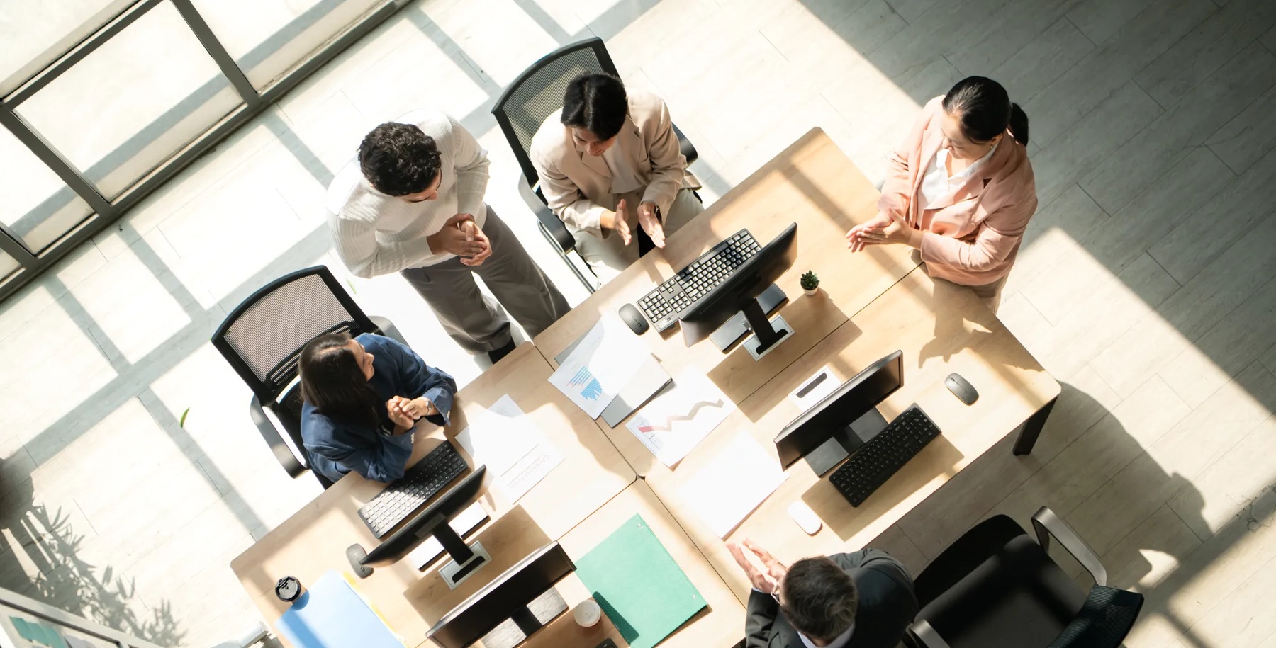 Business team standing around a conference table during meetings, discussing charts and reports under natural light, and congratulating each other on achievements with applause