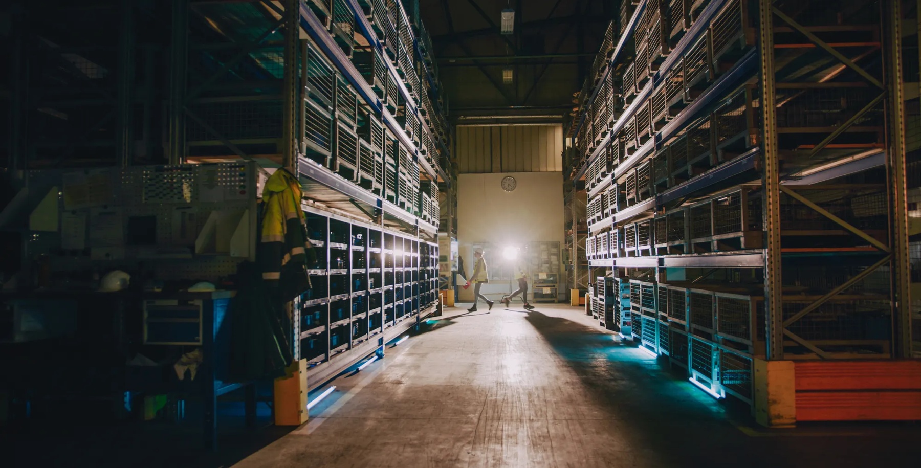 At the distance workers walking at the opposite direction of each other in storage compartment of factory.