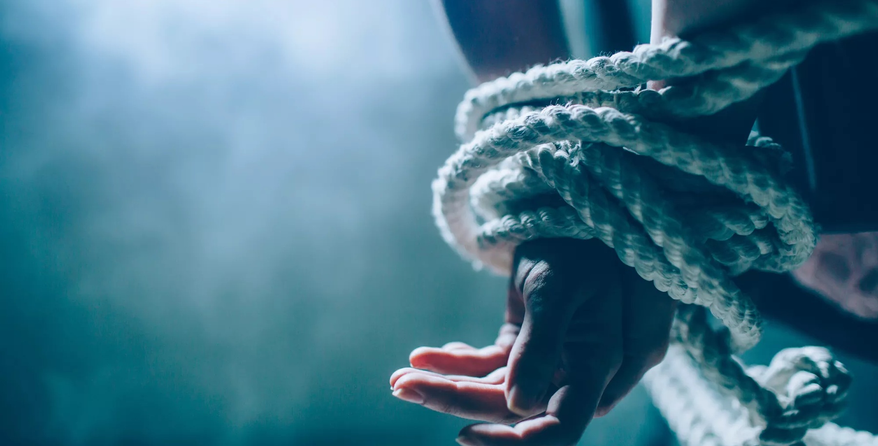 Close up and cut view of woman's hands died in a knot with a rope. One hand is up on another. Woman is tied behind her back. There is a window in dark room. Also there is a white smoke.