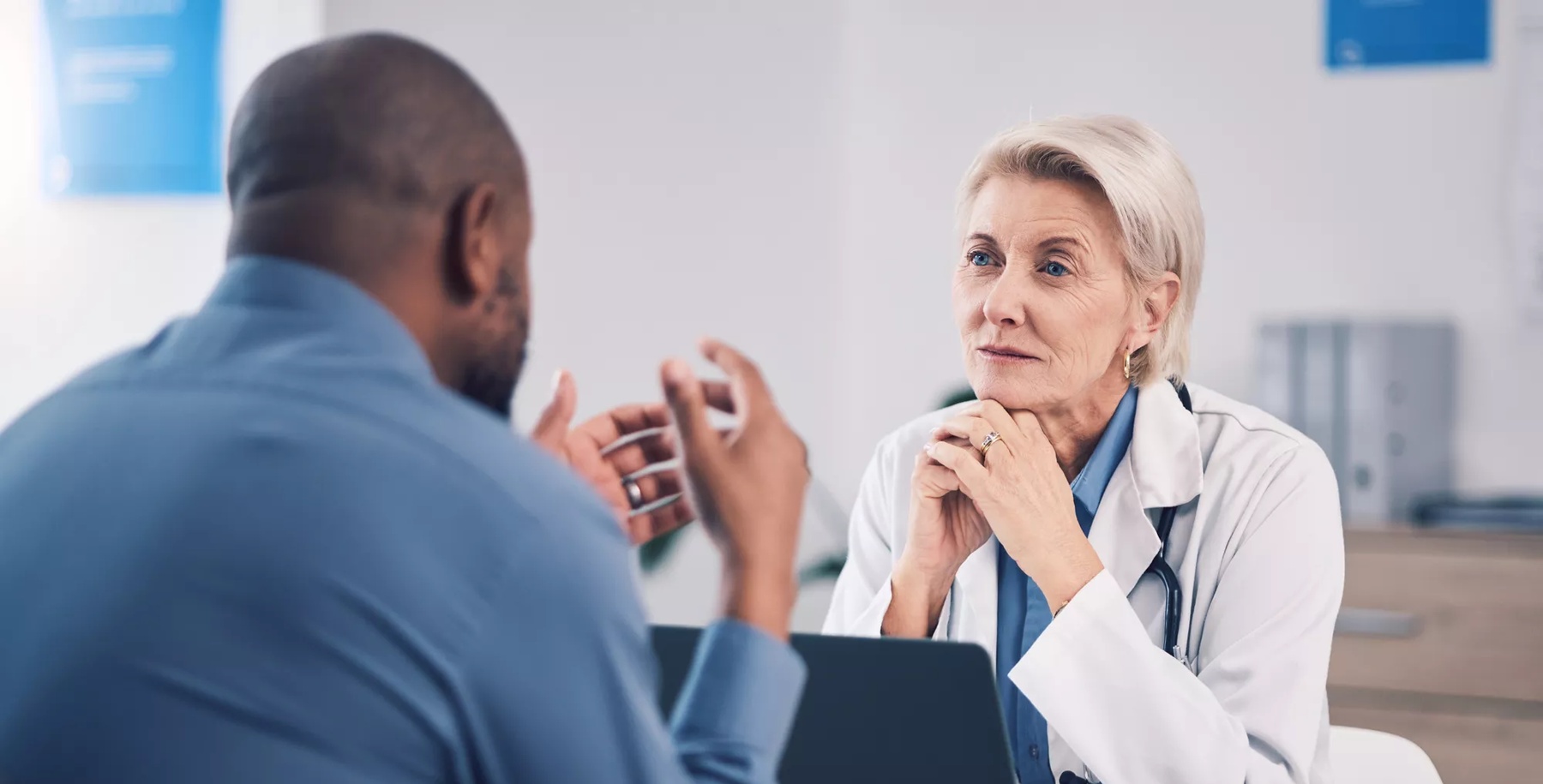 Woman, doctor and listening to man in consultation for healthcare advice at clinic. Mature medical professional consulting with patient for support, wellness services and communication in hospital