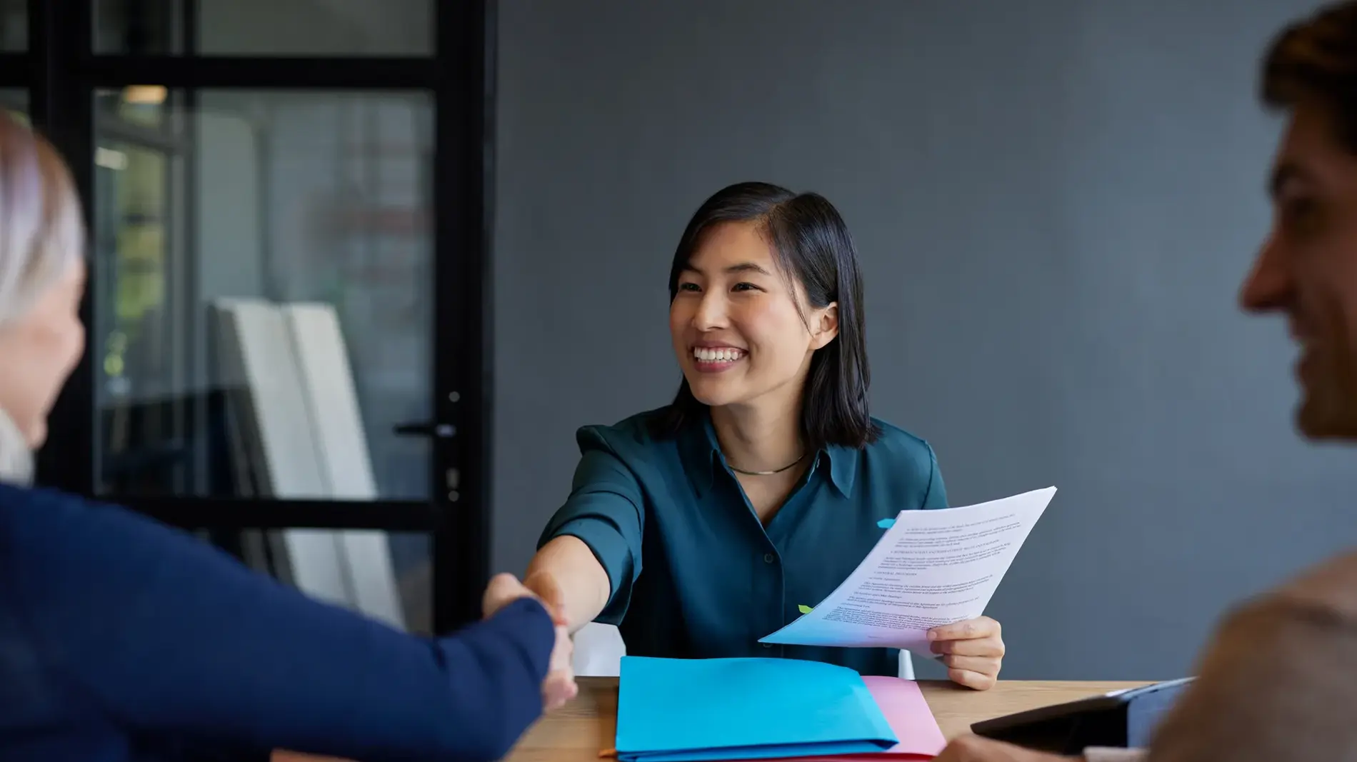 Smiling chinese candidate shakes hands during a job interview with female boss. Professional interview with candidate presenting documents. Financial advisor shaking hands after meeting a couple interested in new investments.