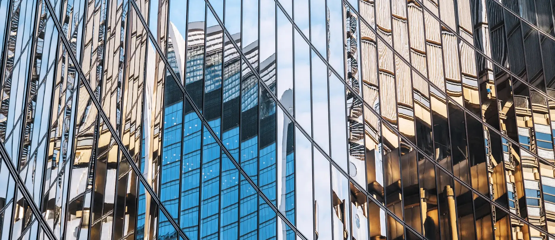 UK, wall features of a steel and glass built Financial Building in London Business District with reflections of city skyscrapers, in early morning sunlight and soft blue sky
