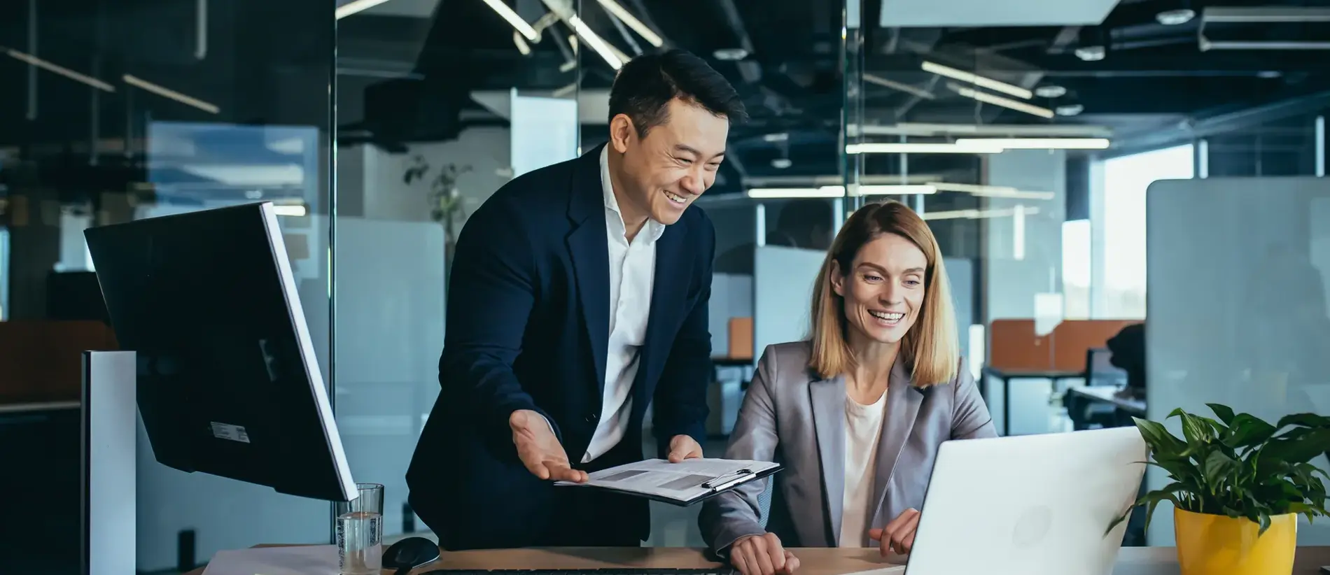 Two employees in a modern office, an Asian man and a woman working at a table, colleagues discussing and consulting, thinking about a joint project