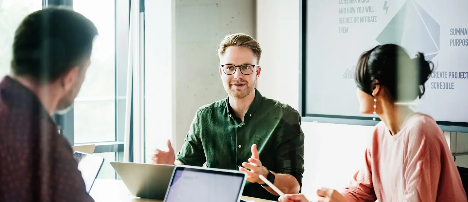 A focused team leader is addressing colleagues in a meeting, with a presentation displayed in the background, capturing a moment of active corporate engagement.