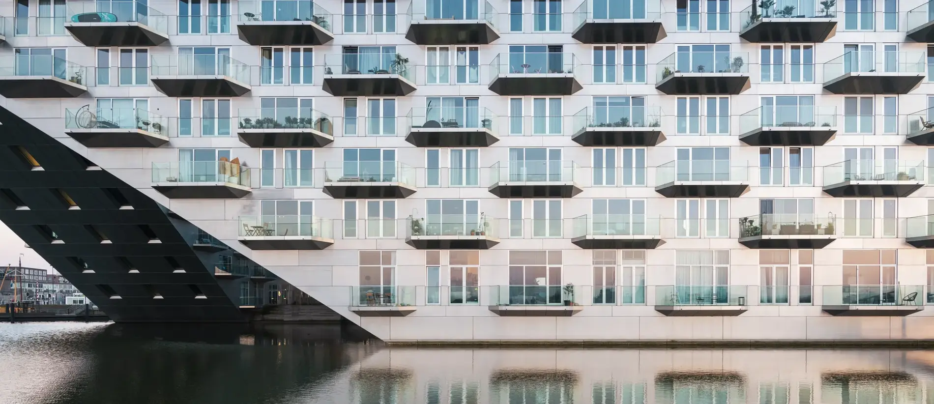 Contemporary architecture with balconies mirrored in still water, creating a symmetrical urban landscape. The building is called Sluishuis, it is entirely built on water and is located on Steigereiland, Amsterdam municipality.