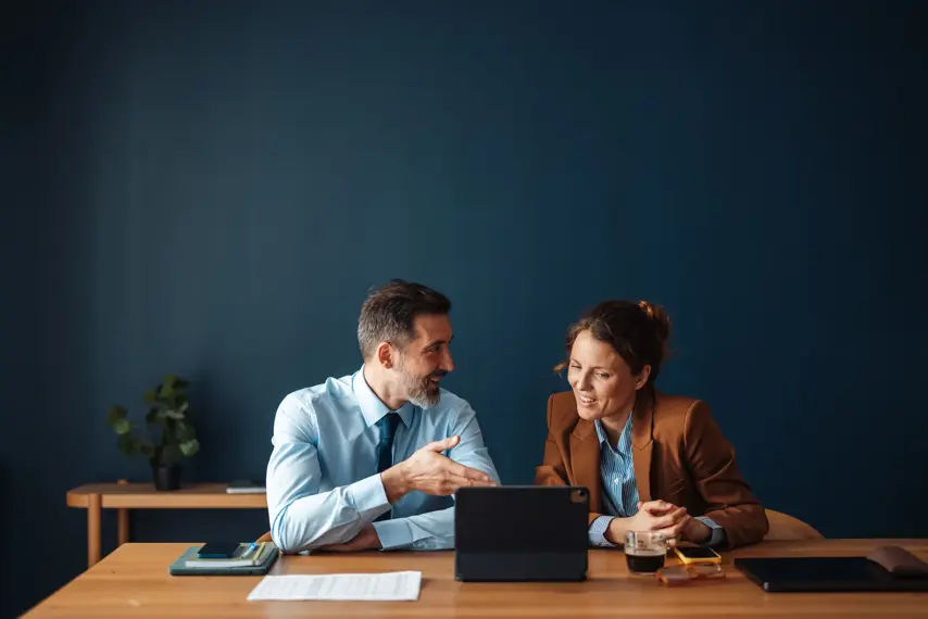 Two engaged colleagues share ideas while seated around a table, highlighting teamwork and collaboration in a modern office setting that fosters creativity and communication.