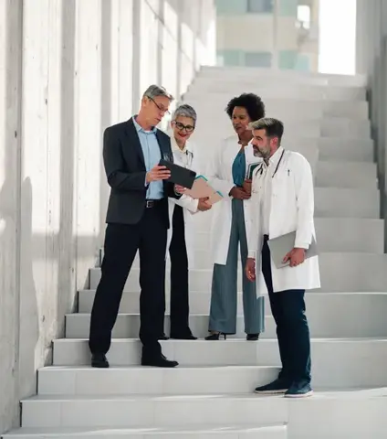 Business man and medical professionals having an important discussion on hospital stairs, collaborating with a digital tablet