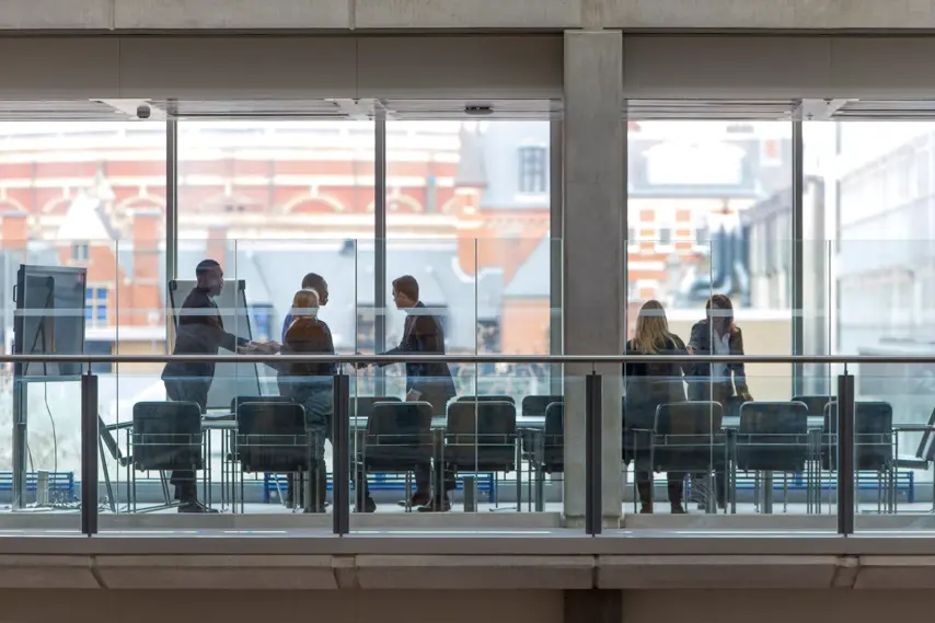 Group of six business people in a boardroom meeting. Shot at a distance from outside through the glass.
