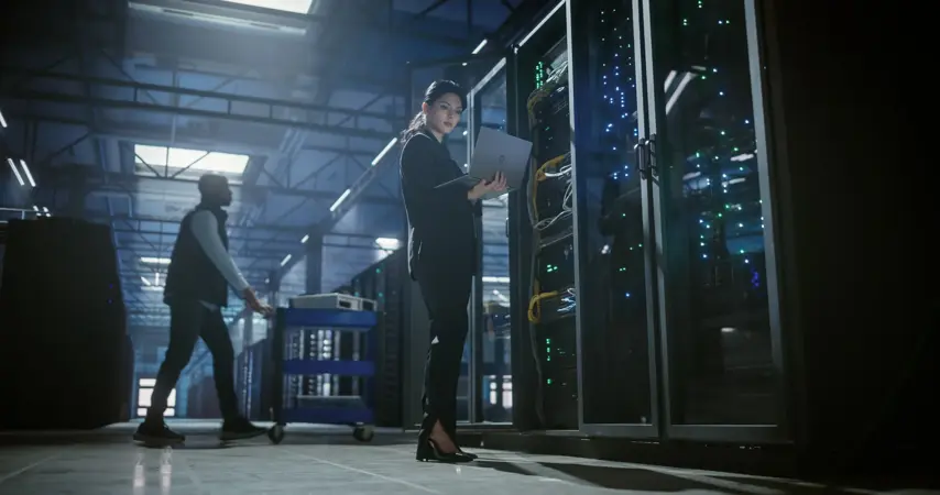 IT engineer uses a laptop to check and monitor server equipment. Software diagnostics, internet connectivity, and technical service support for stable infrastructure and system performance.