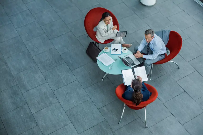 Image of three business people in red chairs around a small conference table.