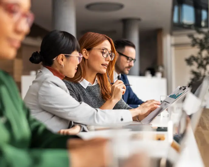 Diverse colleagues engaging in a professional discussion, analyzing documents, demonstrating teamwork in an office setting. Focus on strategy, cooperation, and communication among a business team at work.