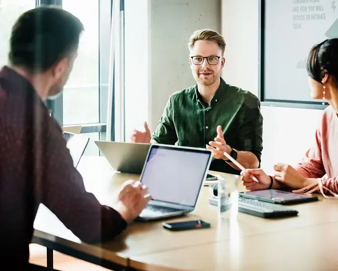 A focused team leader is addressing colleagues in a meeting, with a presentation displayed in the background, capturing a moment of active corporate engagement.