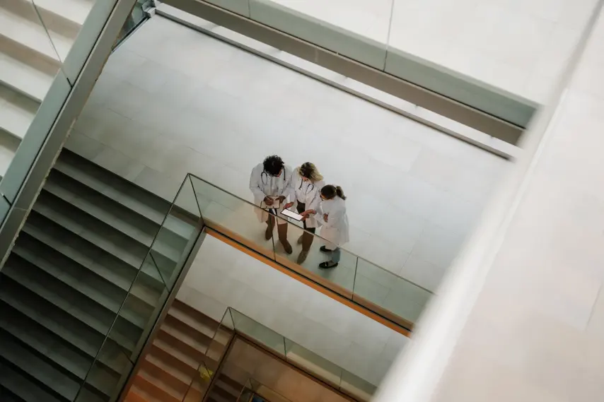 Three doctors collaborating in a modern hospital hallway, analyzing information on a tablet while discussing patient care and treatment options