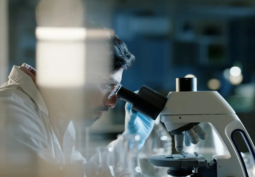 Doctor, microscope and analysis in lab for medical study, scientific innovation and stem cell research. Indian man, investigation and experiment with biotechnology for dna, exam or test for bacteria