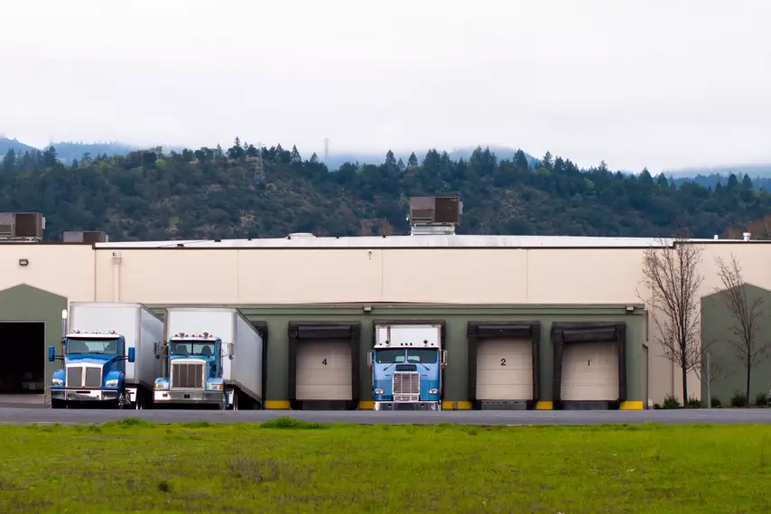 Number of rig semi trucks of various makes and years model of manufacture with trailers are under the loading or unloading of wine production at the docks warehouse in Napa Valley vineyards and winemaking place.