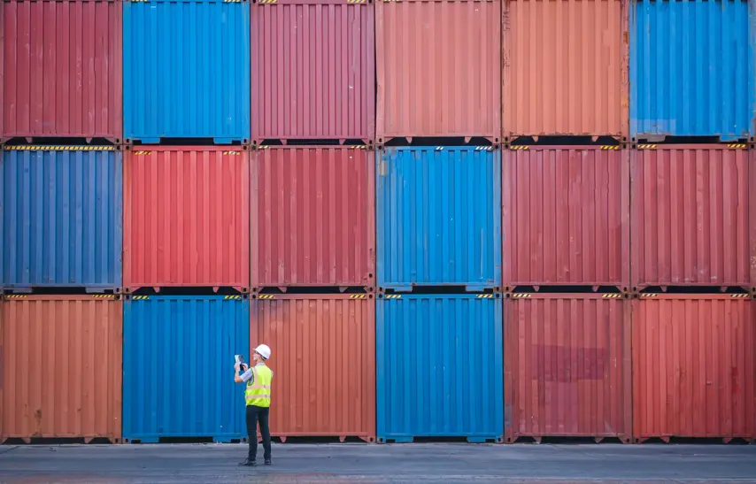 Engineer and tablet at Containers yard from Cargo freight ship for import export. Dock control worker wearing protective coveralls against stack of a containers terminal. Logistic and Transportation, Global Business concepts.