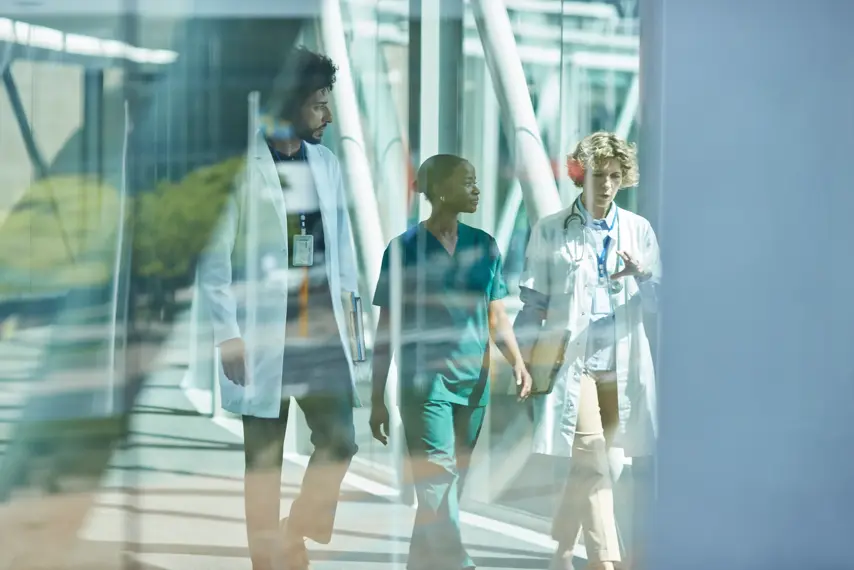Multiracial medical workers discussing while walking on elevated walkway seen through glass